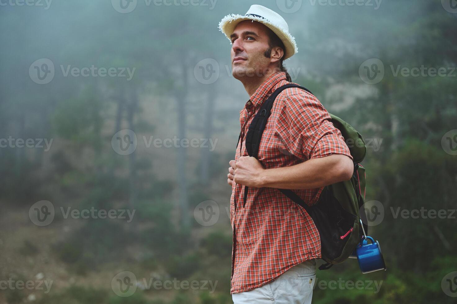 Man hiking in misty forest, wearing hat and backpack, enjoying outdoor adventure and nature exploration photo