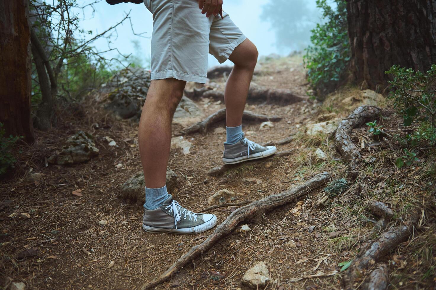 Man hiking on a forest trail wearing sneakers and shorts, surrounded by nature and trees photo