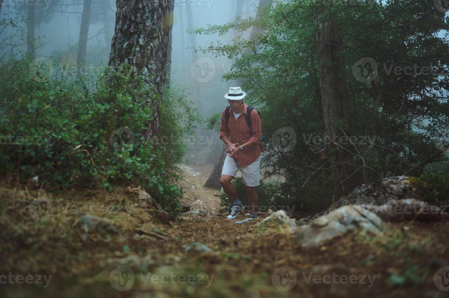 Man hiking in foggy forest wearing hat and backpack, enjoying nature and adventure photo