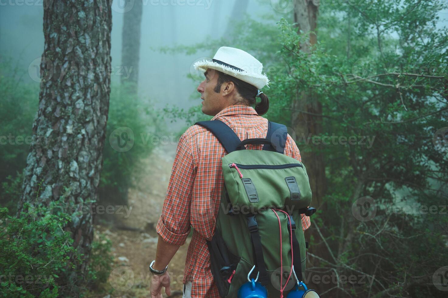 Man hiking in a foggy forest wearing a hat and backpack, exploring nature on a misty morning photo