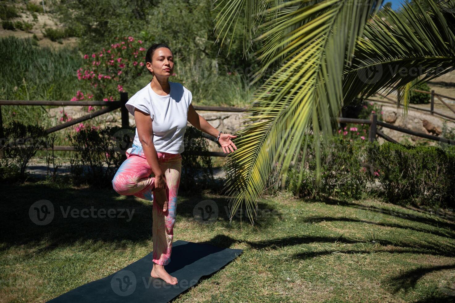 Woman practices yoga in outdoor garden performing tree pose with focus and balance photo