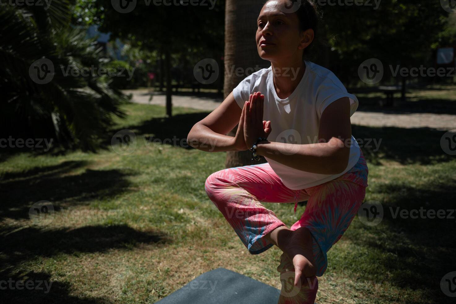 Woman practicing yoga outdoors in park balancing in tree pose under the sunlight photo