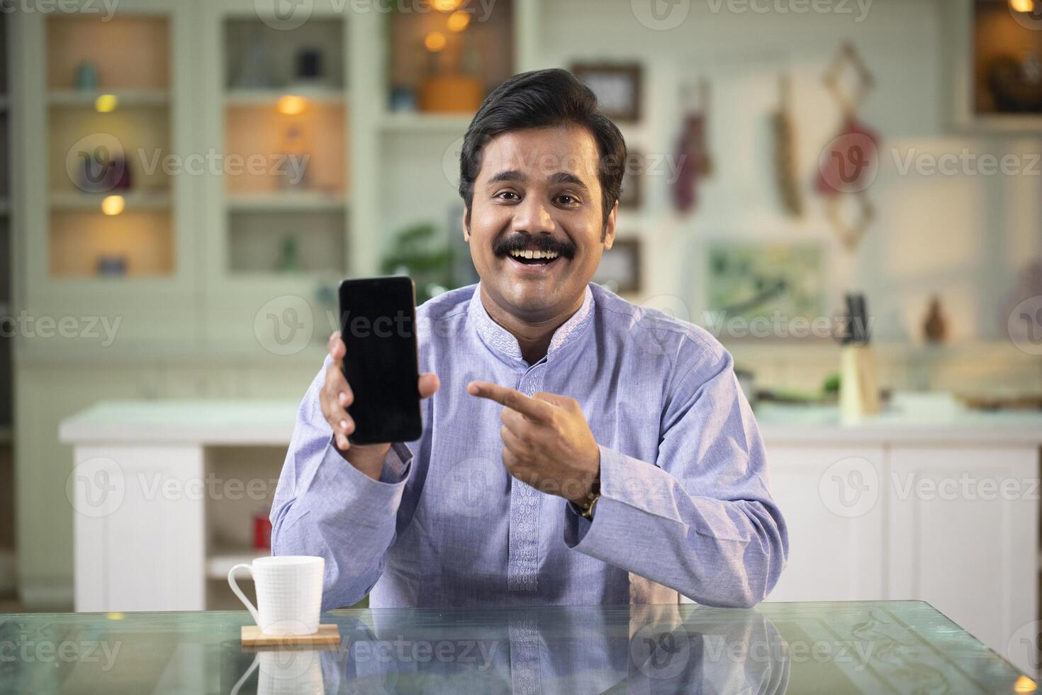 Cheerful Man Looking At Camera Pointing Finger At Empty Phone Screen photo