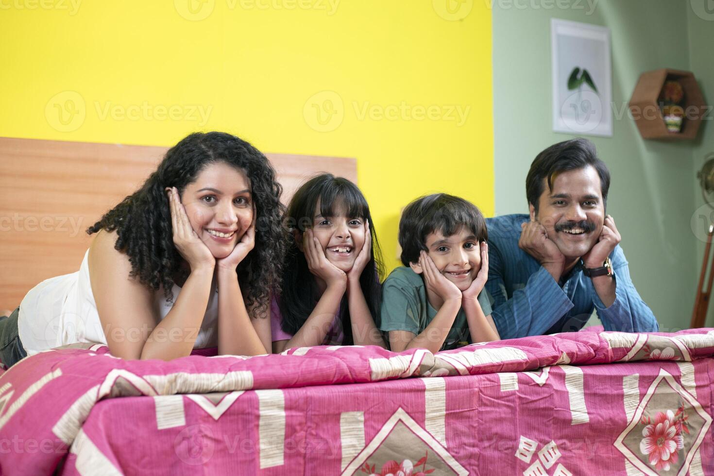Cheerful Family Lying On Bed While Posing In Front Of Camera photo