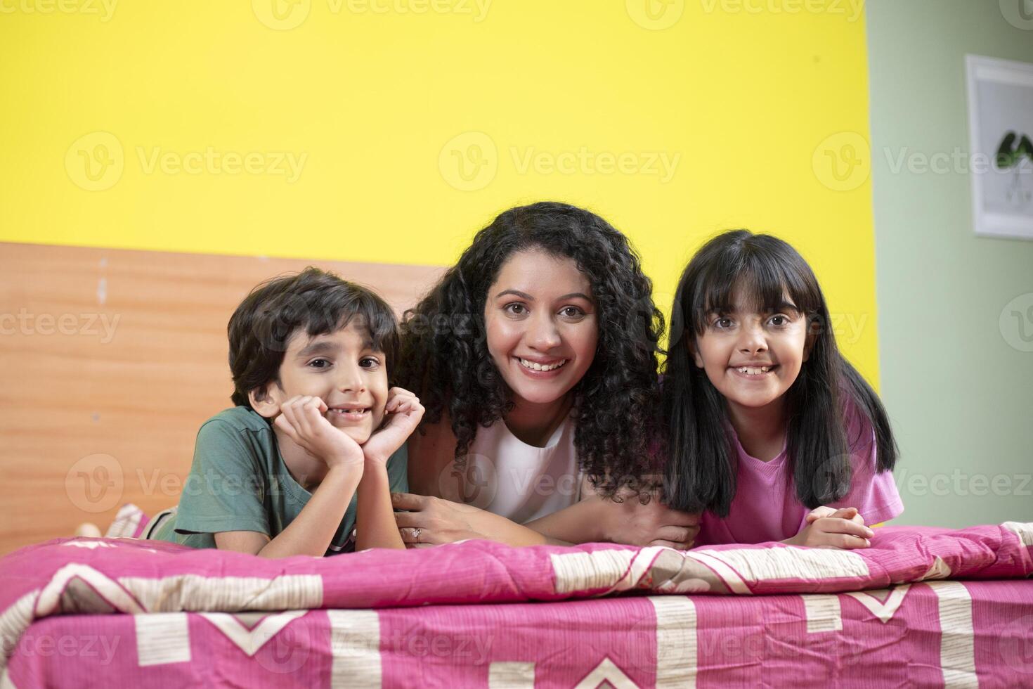 Happy Mom And Her Kids Lying On Bed While Posing In Front Of Camera photo