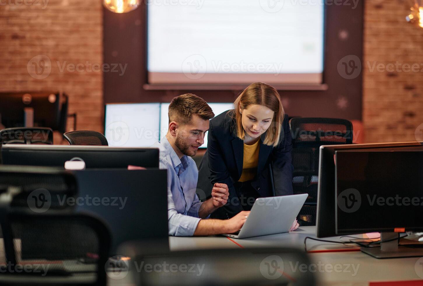 Business colleagues, a man and a woman, engage in discussing business strategies while attentively gazing at a computer monitor, epitomizing collaboration and innovation photo