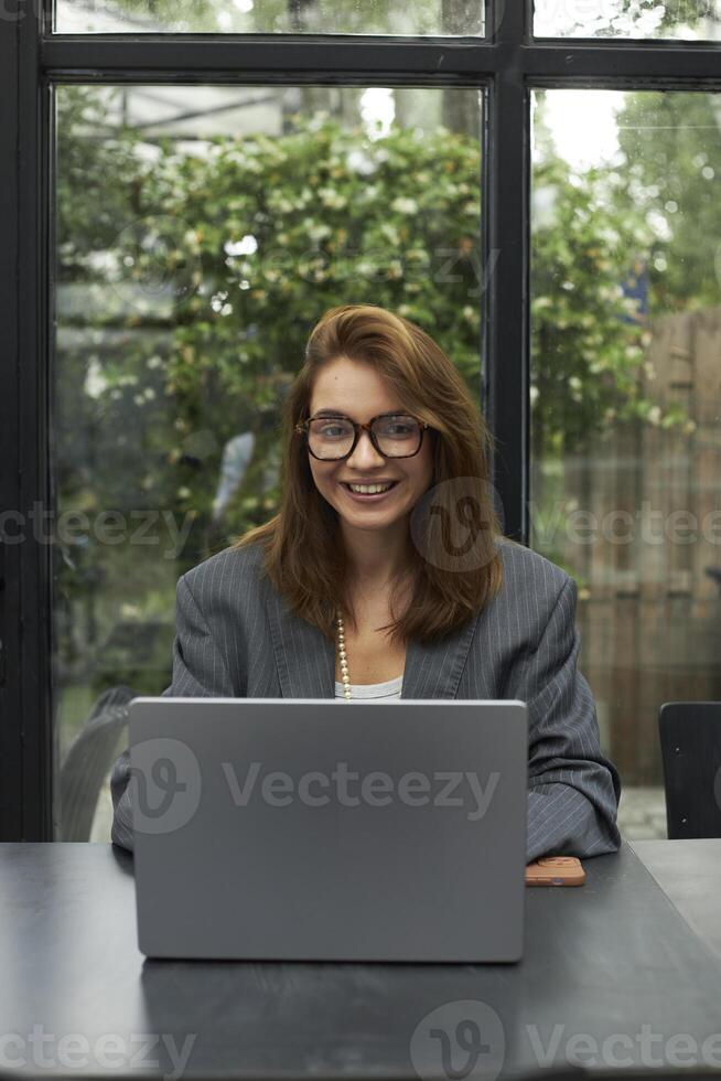 Young woman in eyeglasses working with laptop while sitting at cafe photo