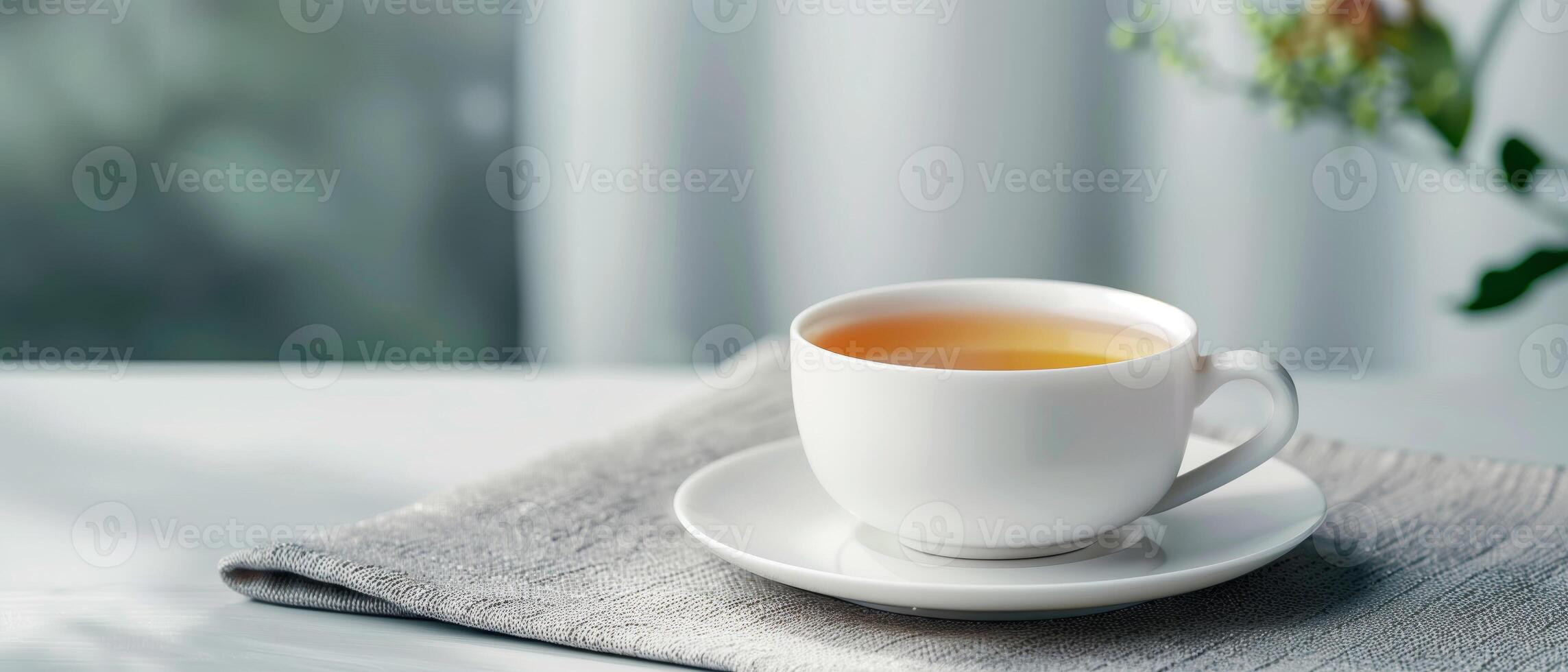 A serene morning moment with a cup of hot tea on a white table, accompanied by a soft gray cloth and natural light. Perfect for relaxation. photo