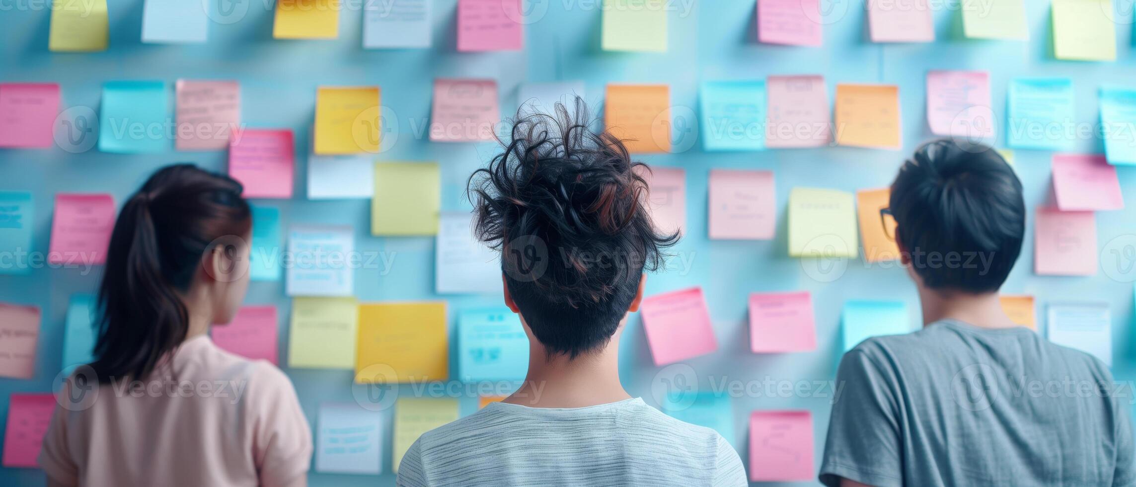 Three people brainstorming in front of a wall covered with colorful sticky notes, discussing ideas and teamwork collaboration. photo