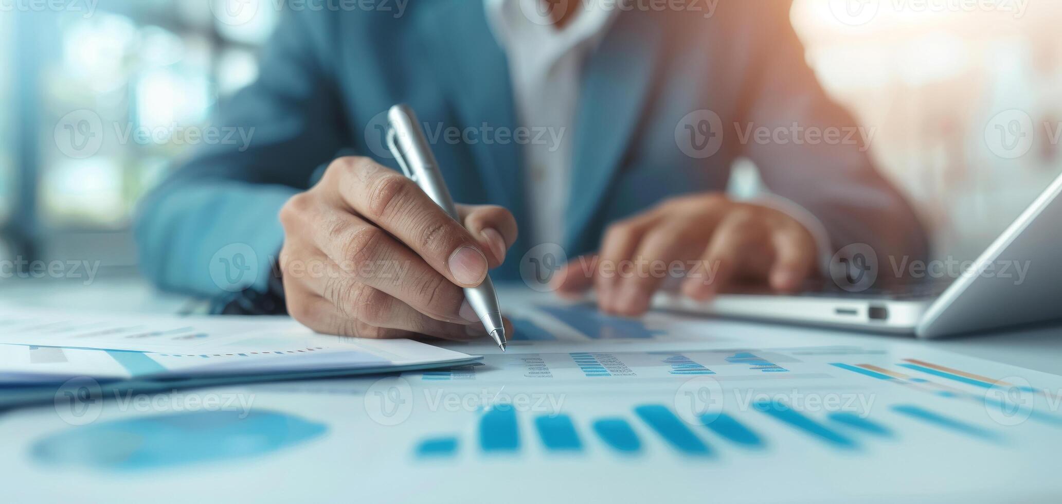 Businessman analyzing financial charts on office desk, using pen and laptop, close-up of hands working on graphs with modern technology. photo
