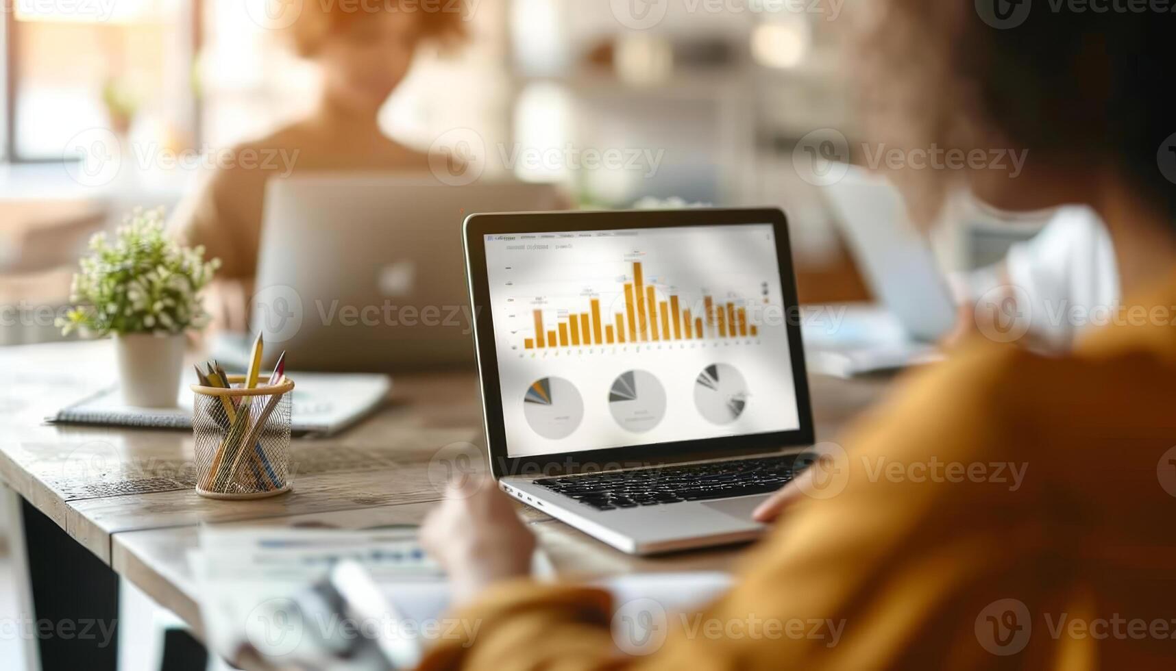 Two people working on laptops in an office setting, one laptop displaying analytical charts and graphs. Focus on data analysis and teamwork. photo