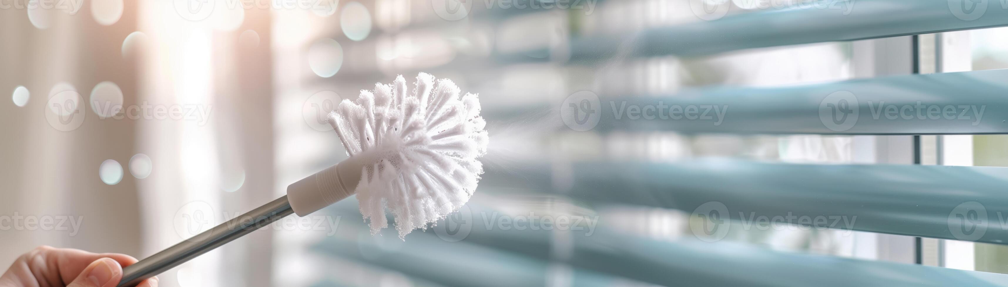 A hand holding a duster, cleaning modern window blinds in a bright and airy room. Ideal for home maintenance and cleaning concepts. photo