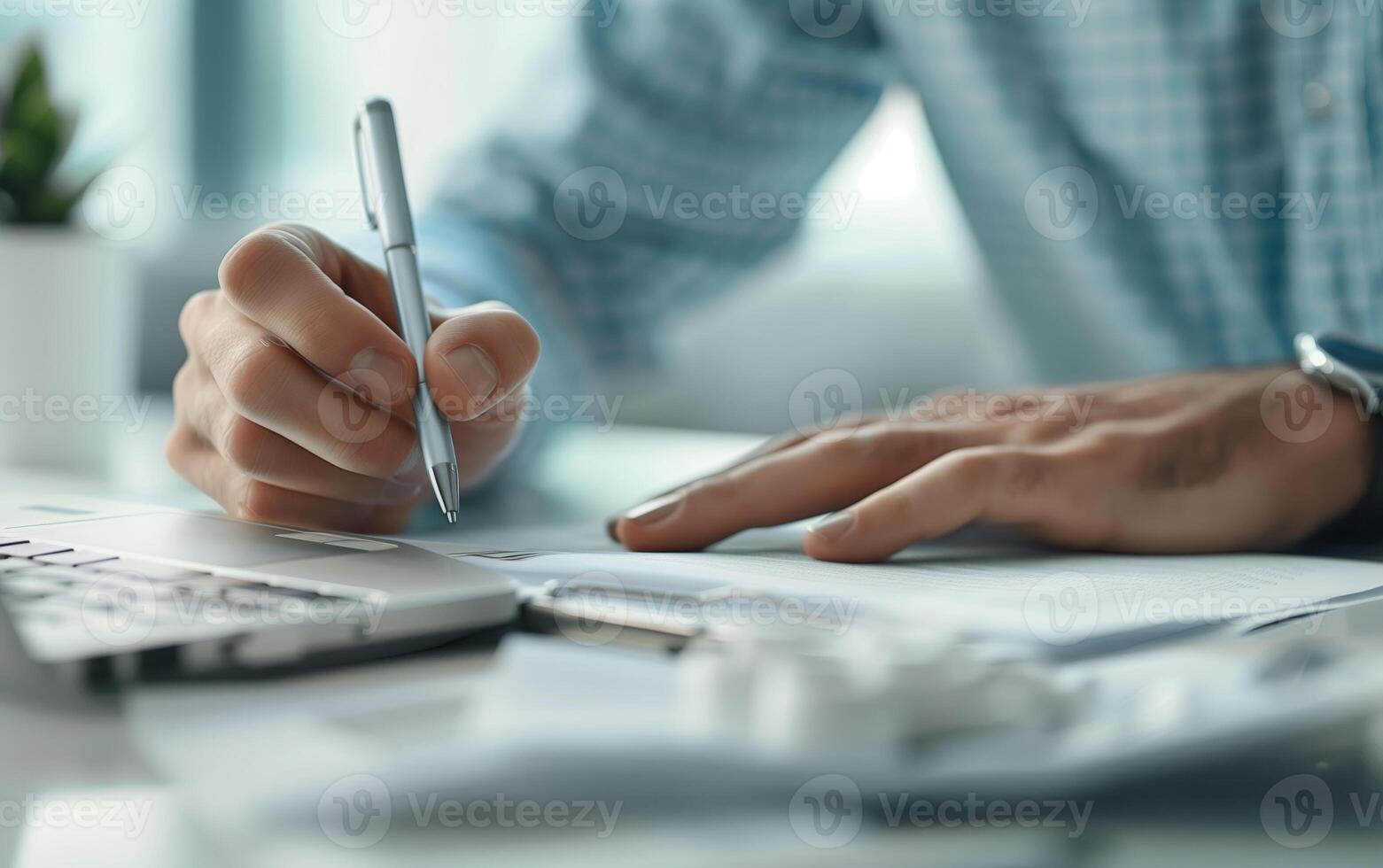Close-up of a person writing at a desk with a laptop and papers, representing business, work, or study in a professional office setting. photo