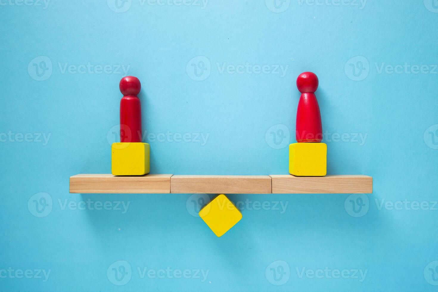 Conceptual image of balance and equality, represented by two red figures balancing on a wooden seesaw photo
