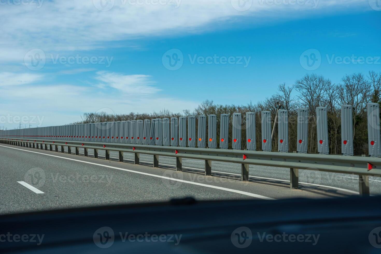 A road with a long line of metal posts with red hearts on them. The road is empty and the sky is clear. photo