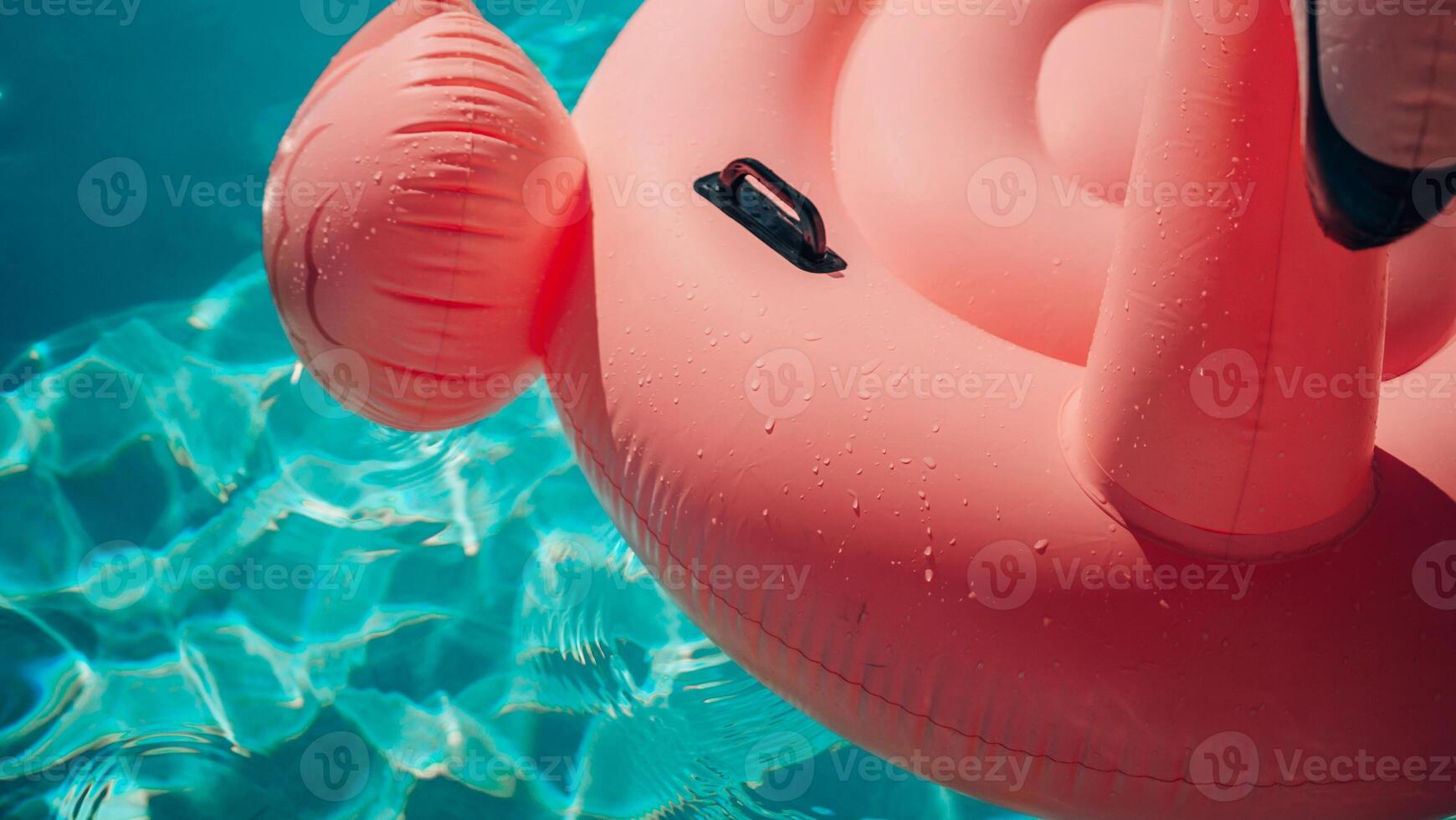 A pink inflatable flamingo is floating in a pool. The water is clear and calm. The flamingo is the main focus of the image, and it is enjoying its time in the water. photo
