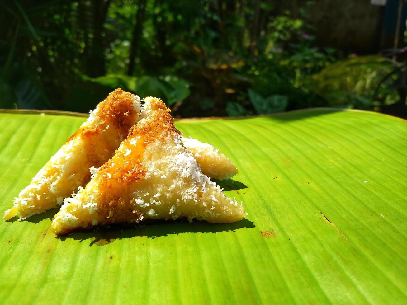 lupis cake is a traditional snack from Indonesia that has a soft and chewy texture made from glutinous rice that has a triangular shape served with grated coconut topping and sweet sauce, street food photo
