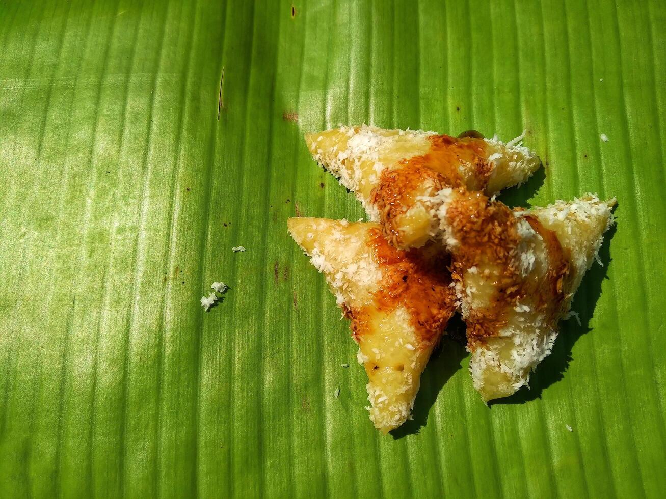 lupis cake is a traditional snack from Indonesia that has a soft and chewy texture made from glutinous rice that has a triangular shape served with grated coconut topping and sweet sauce, street food photo