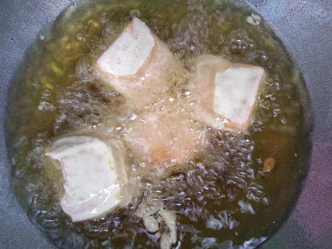 Asian House Wife Frying Tofu on Hot Oil, Using Gas Stove in the Kitchen. Cooking Process Backstage Making Delicious Tahu Goreng photo