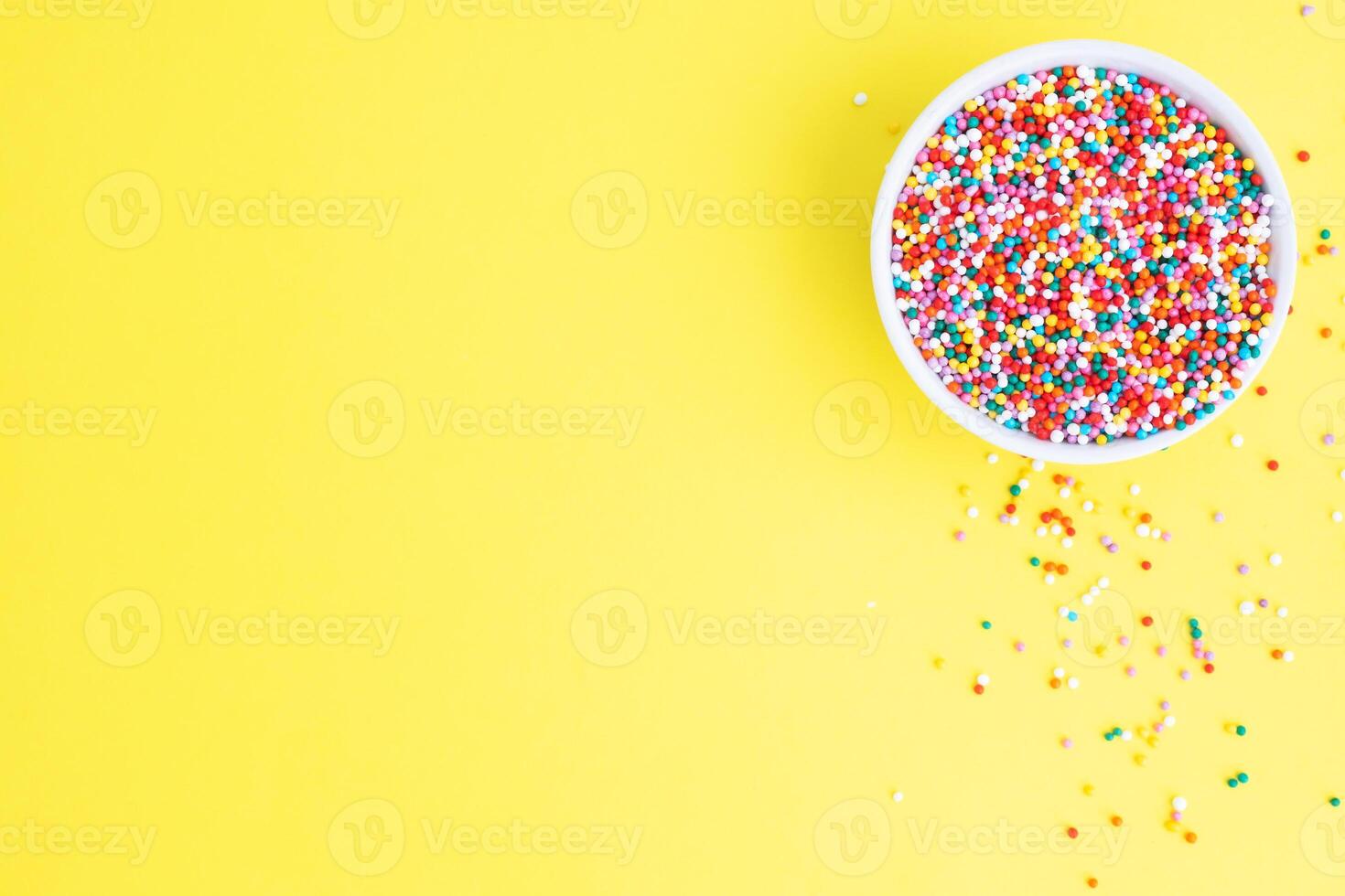 Confectionery sprinkles colored glazed sugar in a plate, top view. copy space Yellow background photo