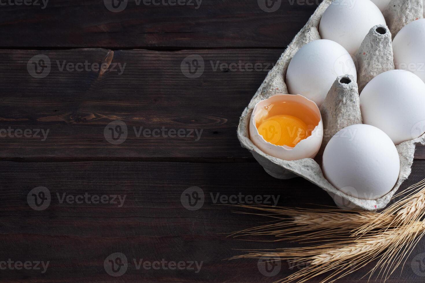 Fresh chicken eggs in a package, raw eggs in a white shell in a box. Top view copy space, wooden background. Broken egg with yolk. photo