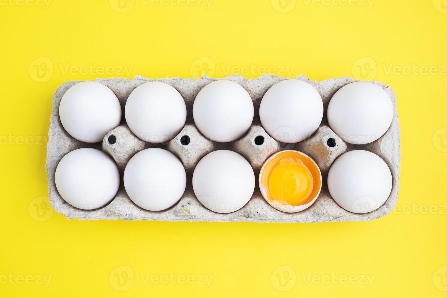Fresh chicken eggs in a package, raw eggs in a white shell in a box. Top view copy space, Yellow background. Broken egg with yolk. photo