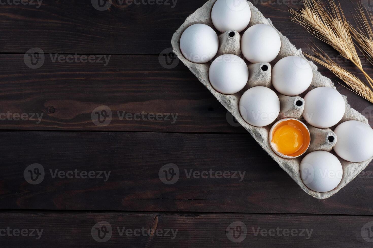 Fresh chicken eggs in a package, raw eggs in a white shell in a box. Top view copy space, wooden background. Broken egg with yolk. photo