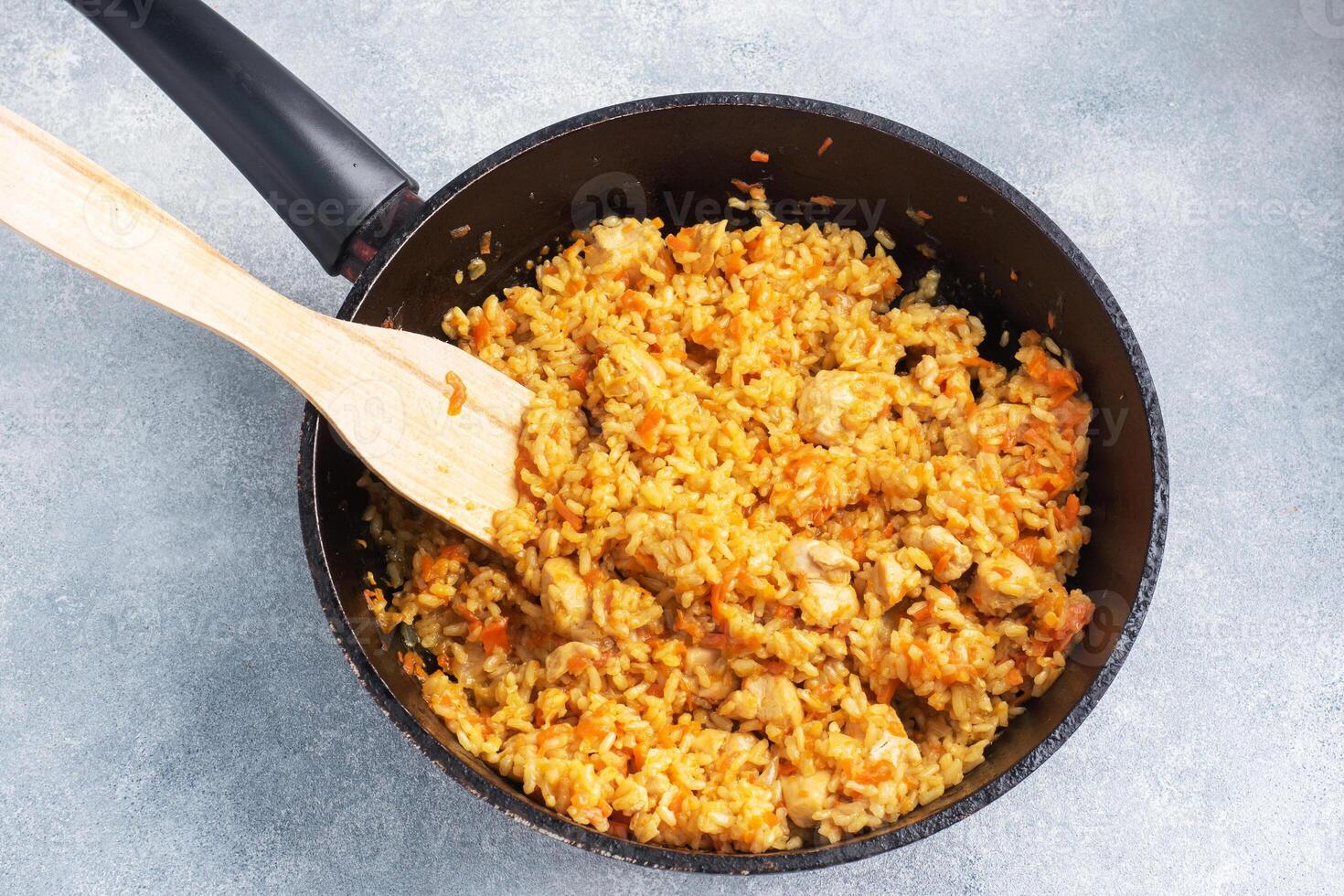 Delicious Asian pilaf, stewed rice with vegetables and chicken in a frying pan. gray concrete background. copy space. photo