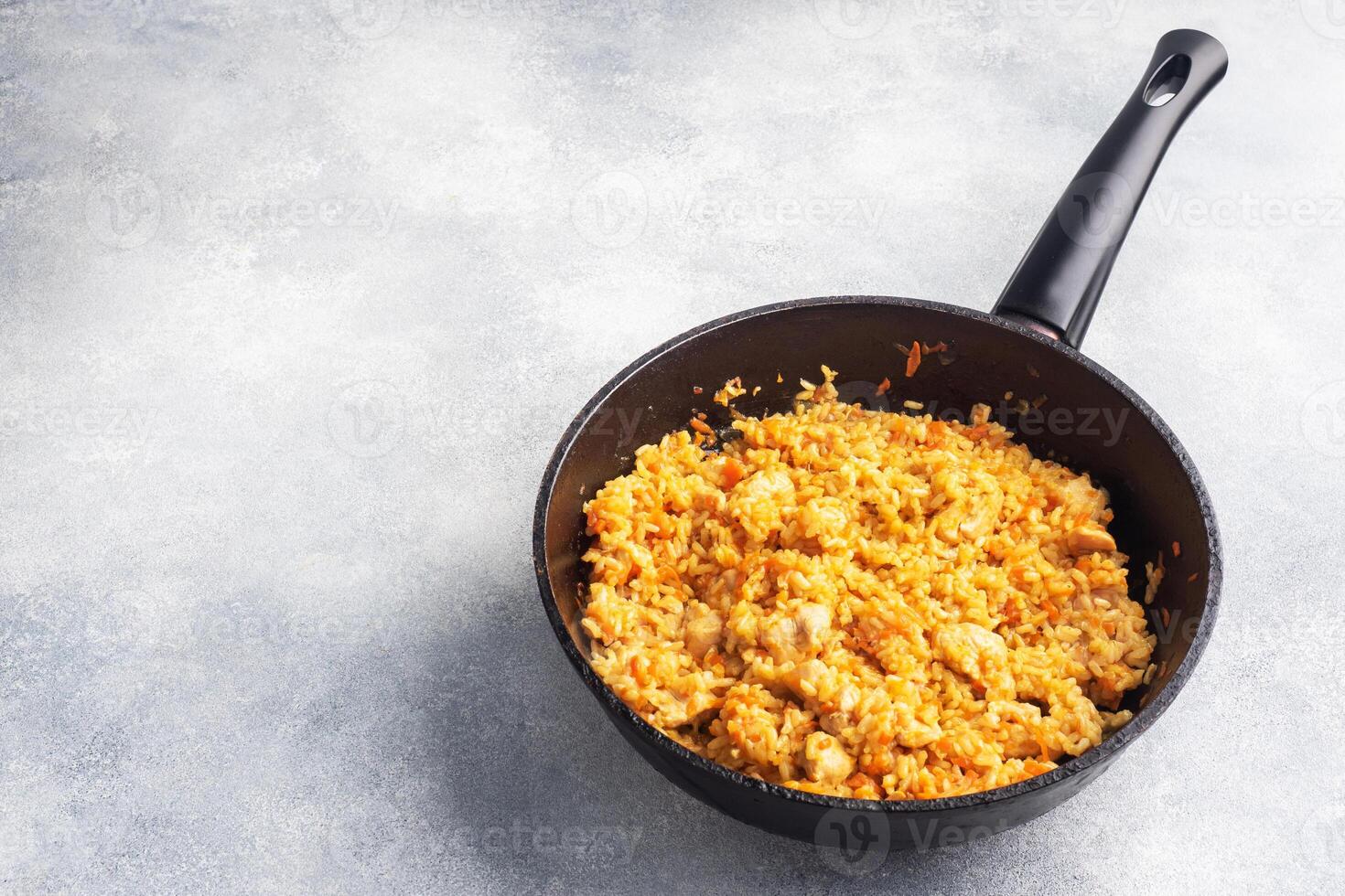 Delicious Asian pilaf, stewed rice with vegetables and chicken in a frying pan. gray concrete background. copy space. photo