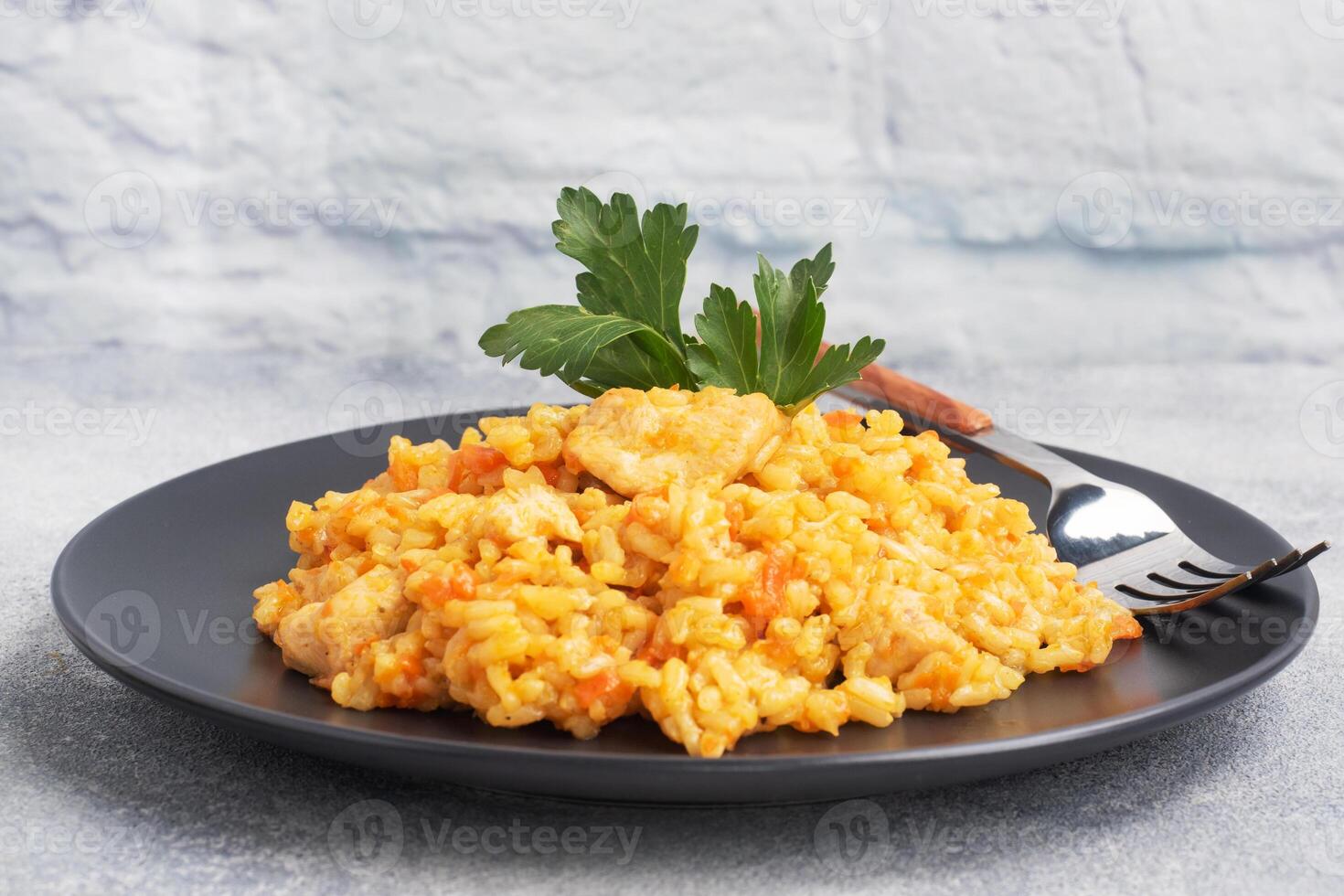 Delicious Asian pilaf, stewed rice with vegetables and chicken on a plate. gray concrete background. copy space. photo