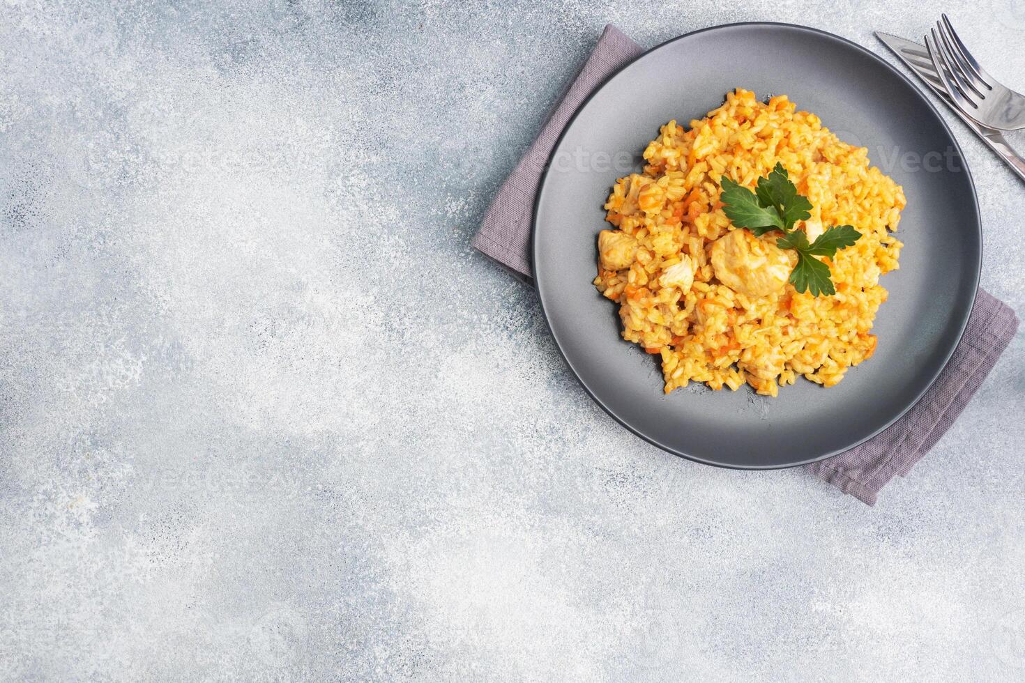 Delicious Asian pilaf, stewed rice with vegetables and chicken on a plate. gray concrete background. copy space. photo
