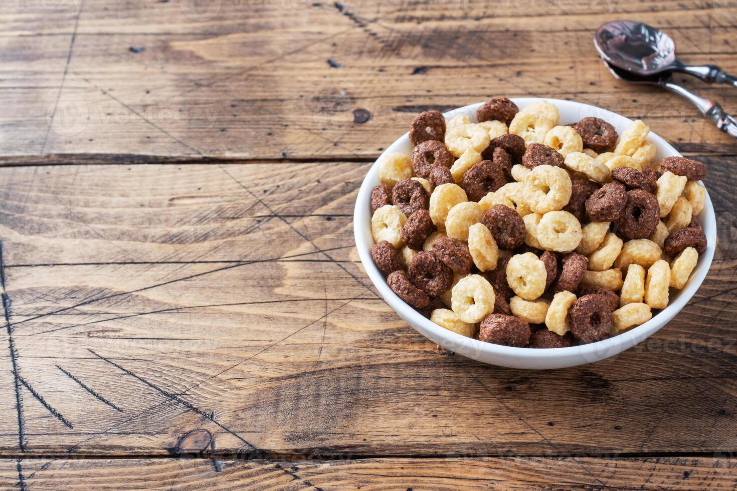 Dry breakfast cereals. Chocolate and corn rings made from natural cereals with milk in a plate. Wooden rustic background, copy space. photo