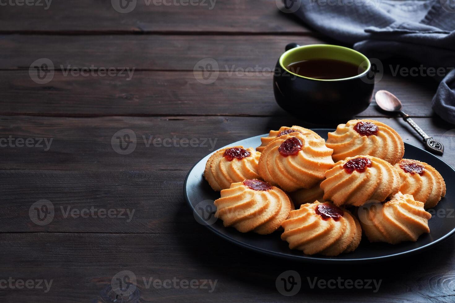 Kurabye shortbread cookies with berry jam in a black plate. Delicious dessert, dark wooden background with copy space. photo