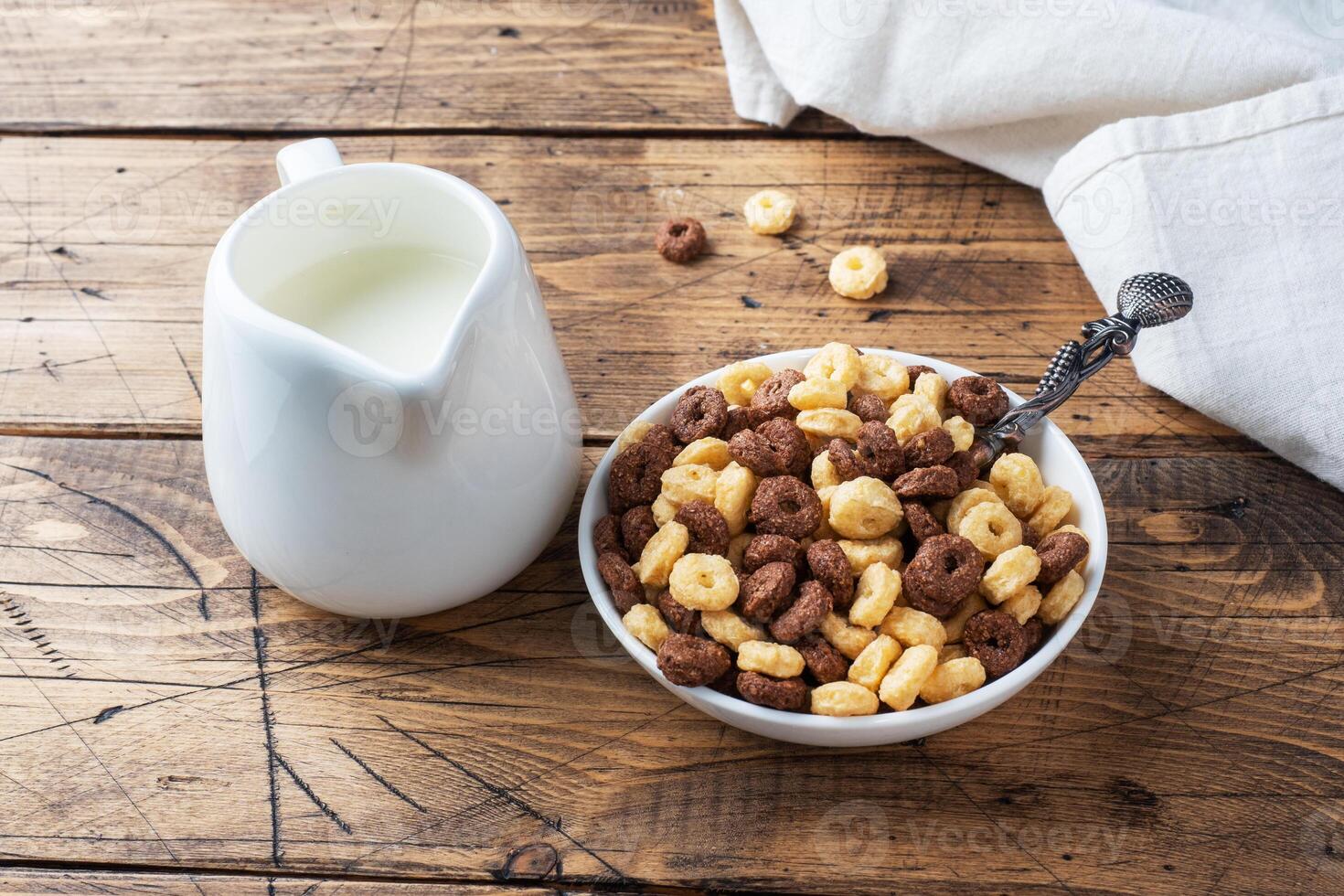 Dry breakfast cereals. Chocolate and corn rings made from natural cereals with milk in a plate. Wooden rustic background, copy space. photo