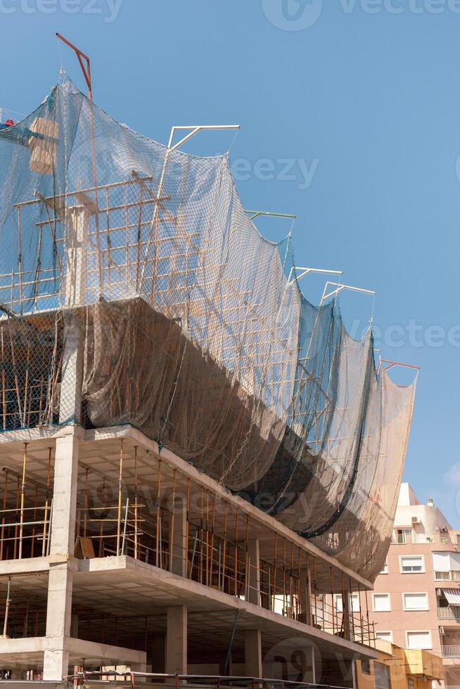 New building construction process. Safety nets and structural beams highlight ongoing work. Detailed shot of multi-level architecture. Ideal for articles on urban development, real estate investment. photo