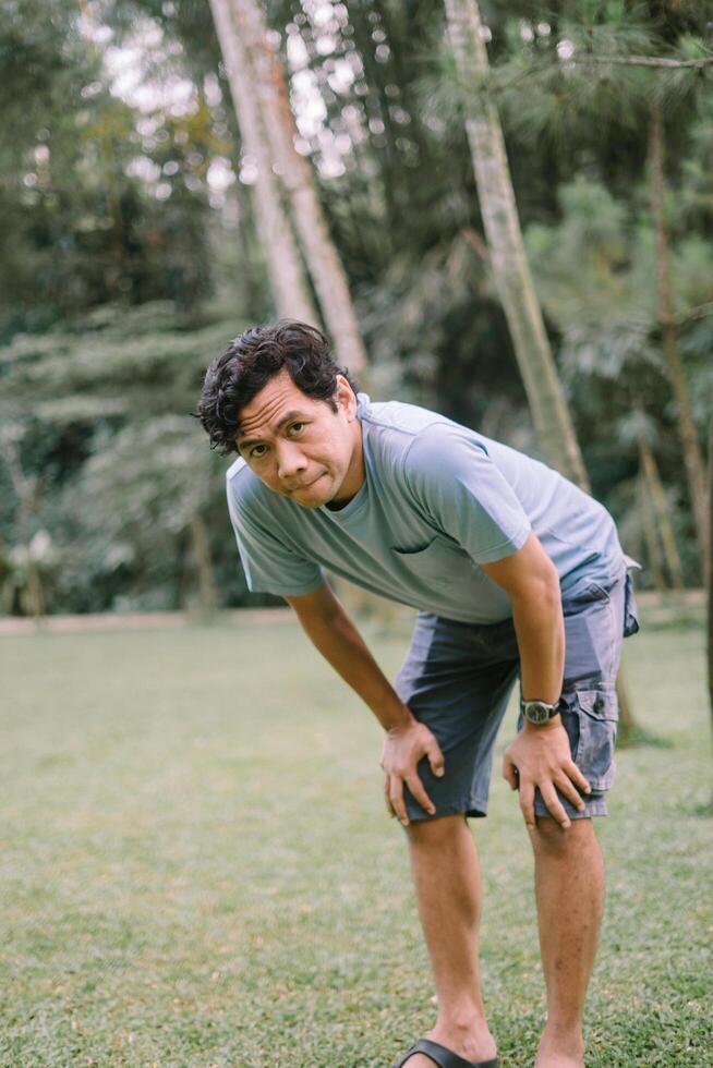 A Southeast Asian man bending over and holding his knees, capturing a moment of exhaustion or effort photo