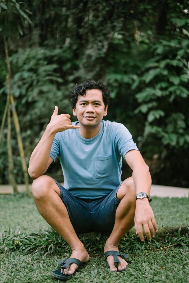 A Southeast Asian man makes a hand gesture as if talking on a phone, conveying a playful and communicative moment photo