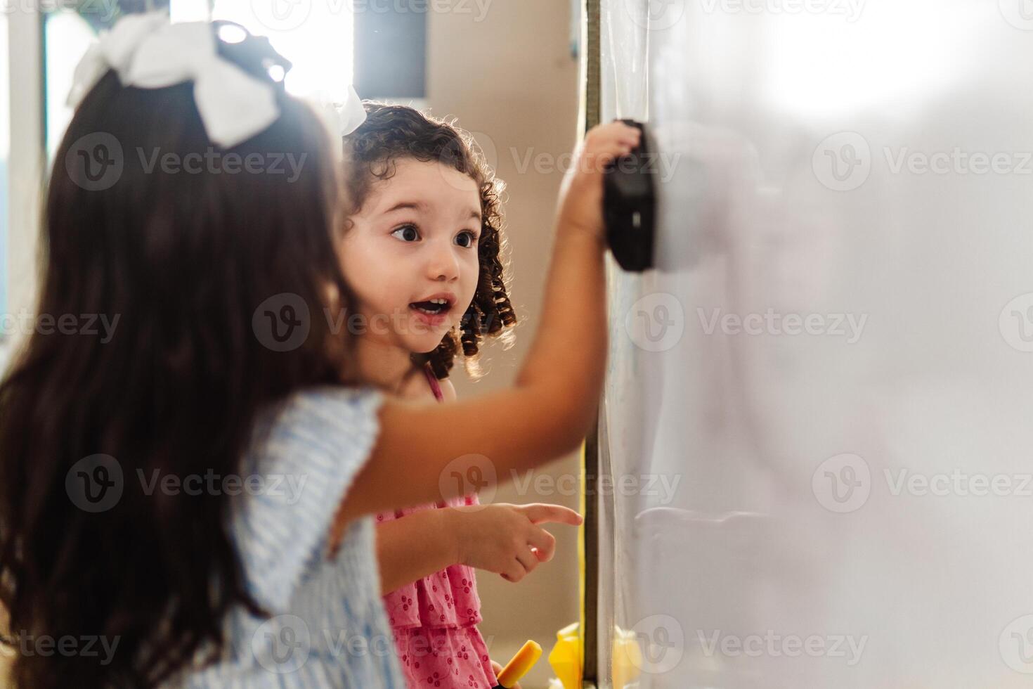 two little girls preschoolar friends front a whiteboard learning in a class. photo