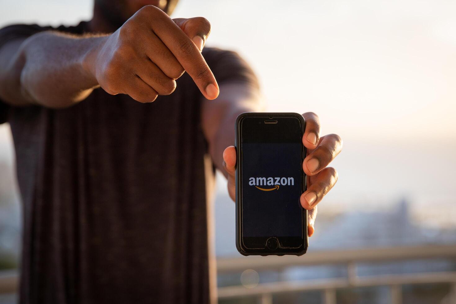 A man holds a smartphone with the Amazon logo. is an American multinational technology company which focuses on e-commerce, cloud computing, digital streaming, and artificial intelligence. photo