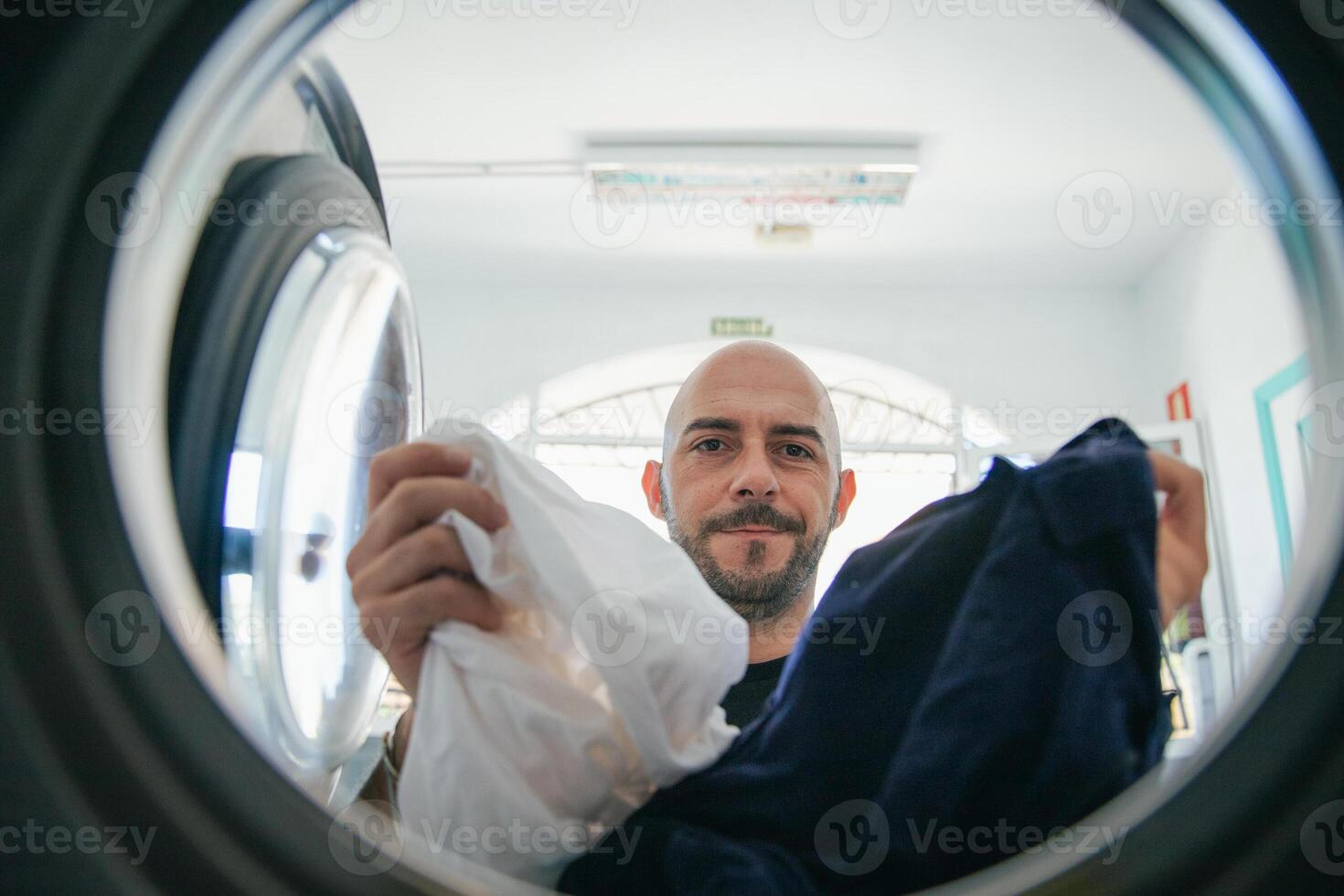 A man loads the washing machine with dirty clothes in the laundromat photo