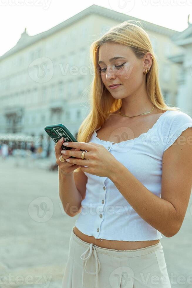 A young woman uses her smartphone while out in the city in summer photo