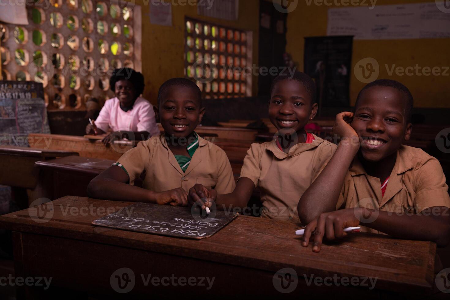 Group of three black children sitting in the classroom with the teacher sitting behind photo