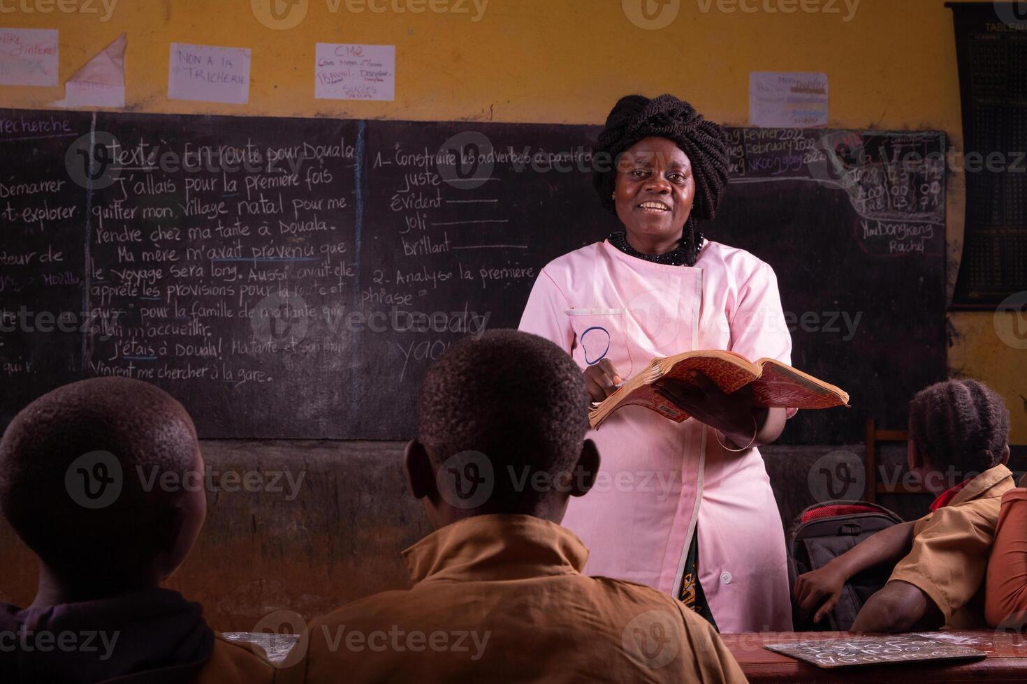 Black female teacher stands in front, explains the lesson by reading from the book from the desk photo