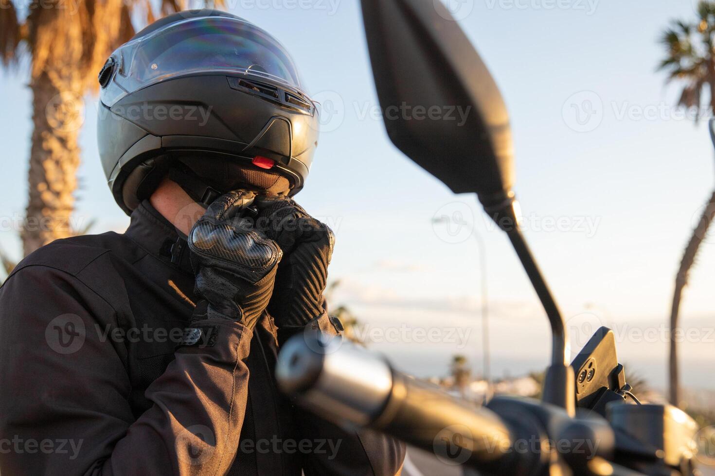 A motorcyclist puts on his helmet and fastens its belt, road safety concept. photo