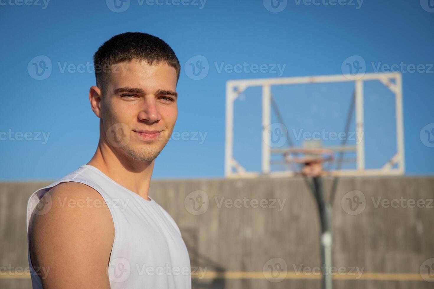 A smiling basketball player on a basketball court with a hoop behind