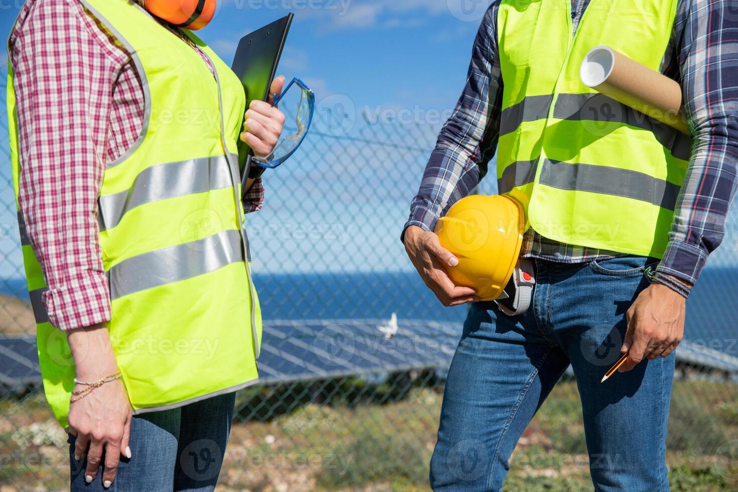 Close-up of the bodies of two engineers wearing reflective vest and holding work tools photo