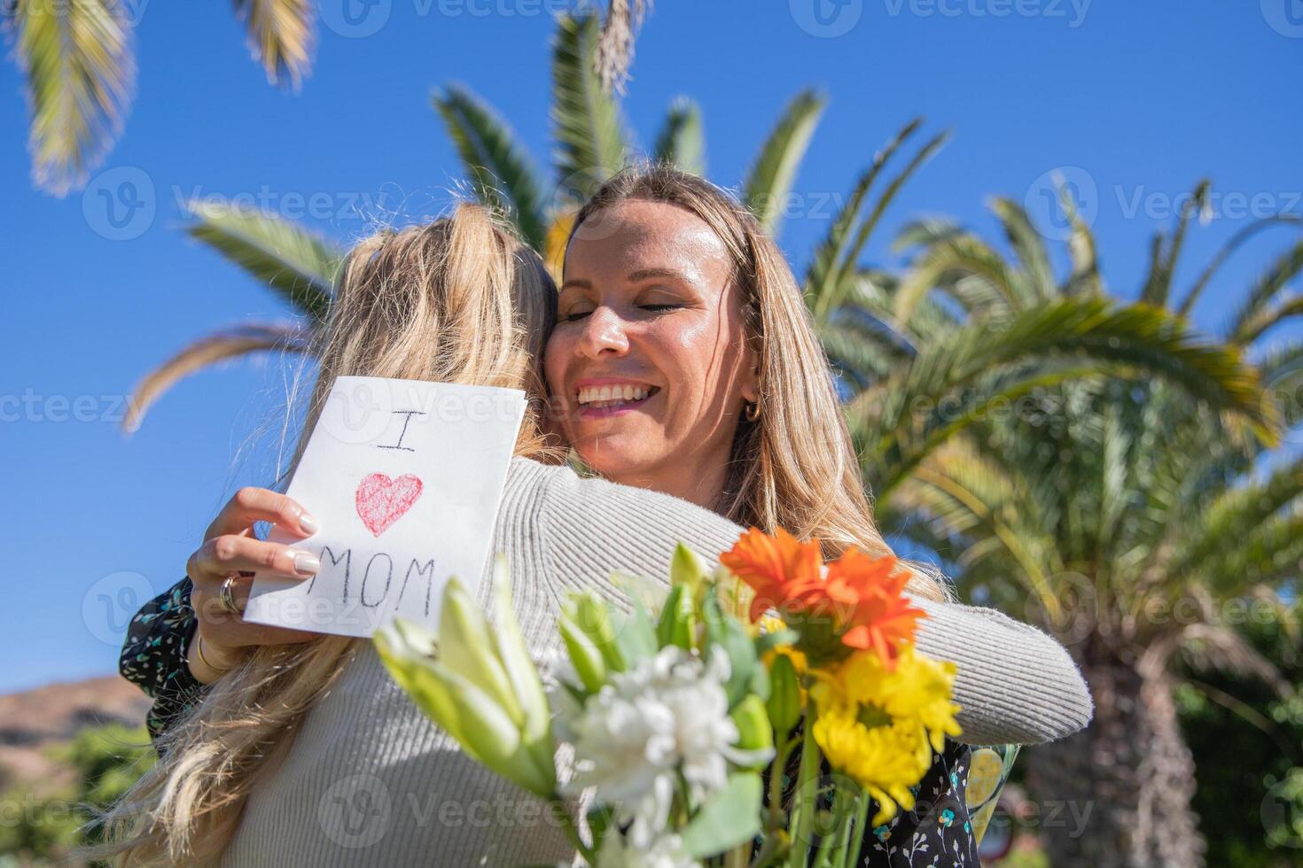 Smiling mother hugs her daughter who celebrates her on mother's day with a card and flowers photo