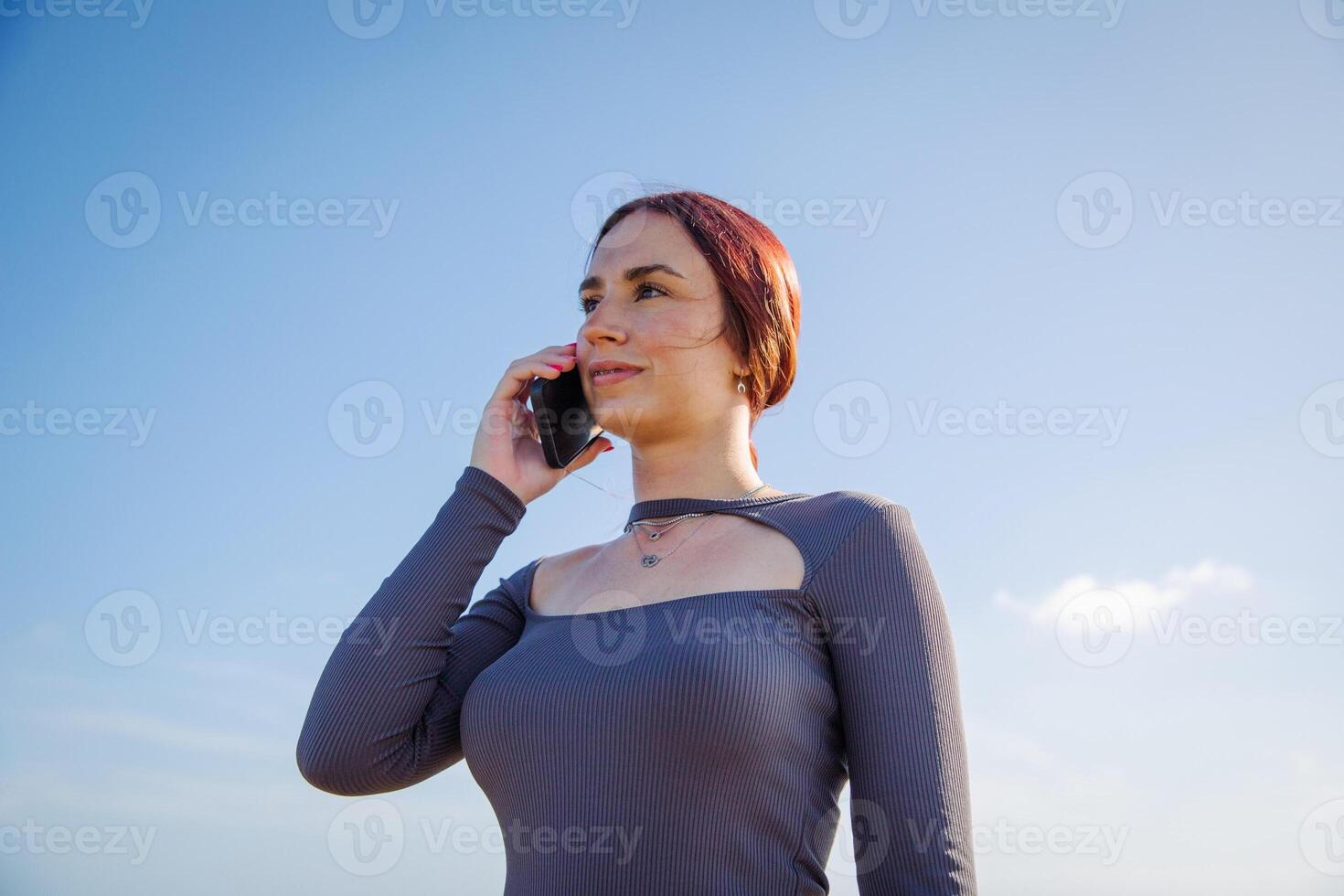 A young woman makes a phone call with the clear sky as background photo