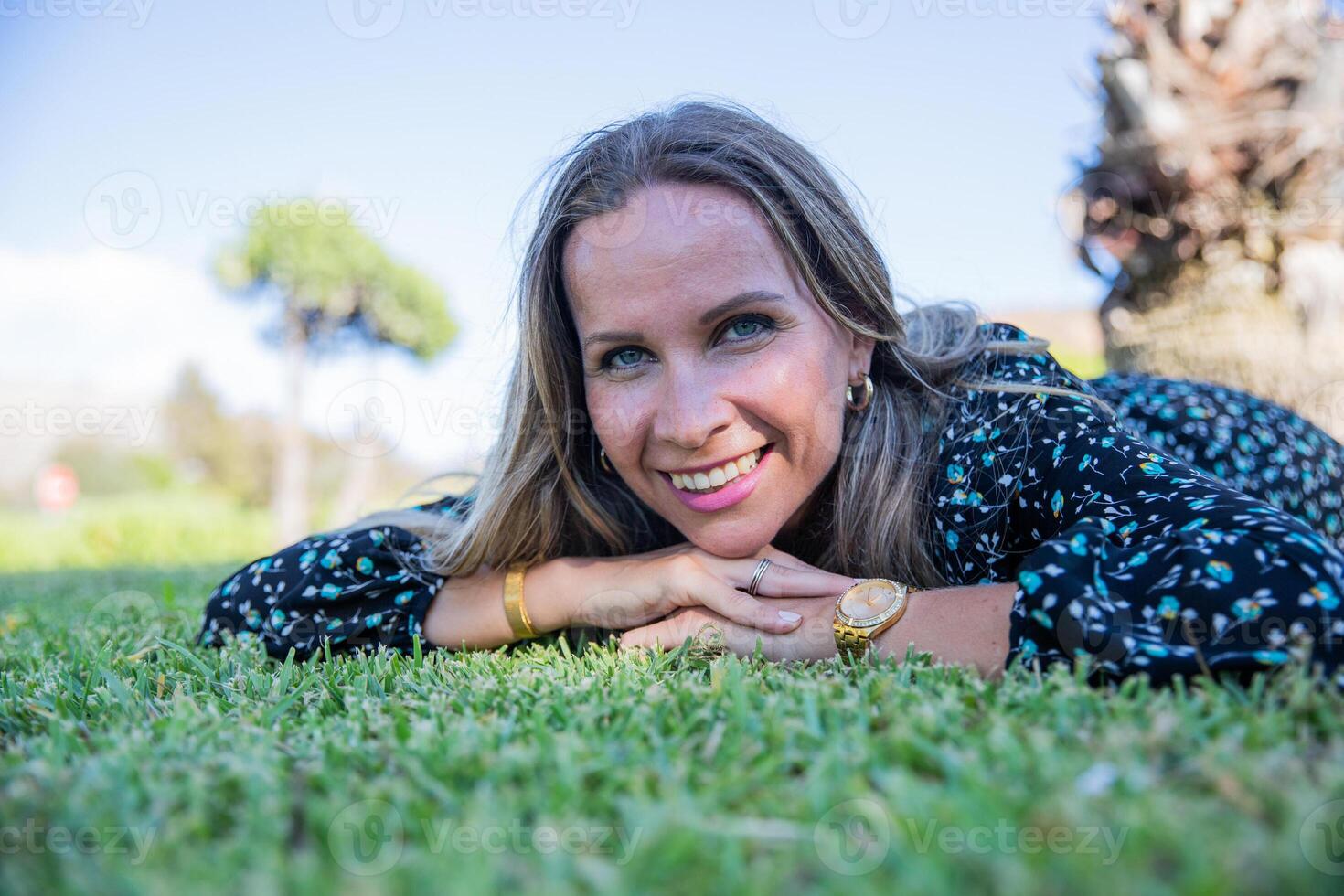 Portrait of a smiling woman laying on the grass with her face on her hands photo