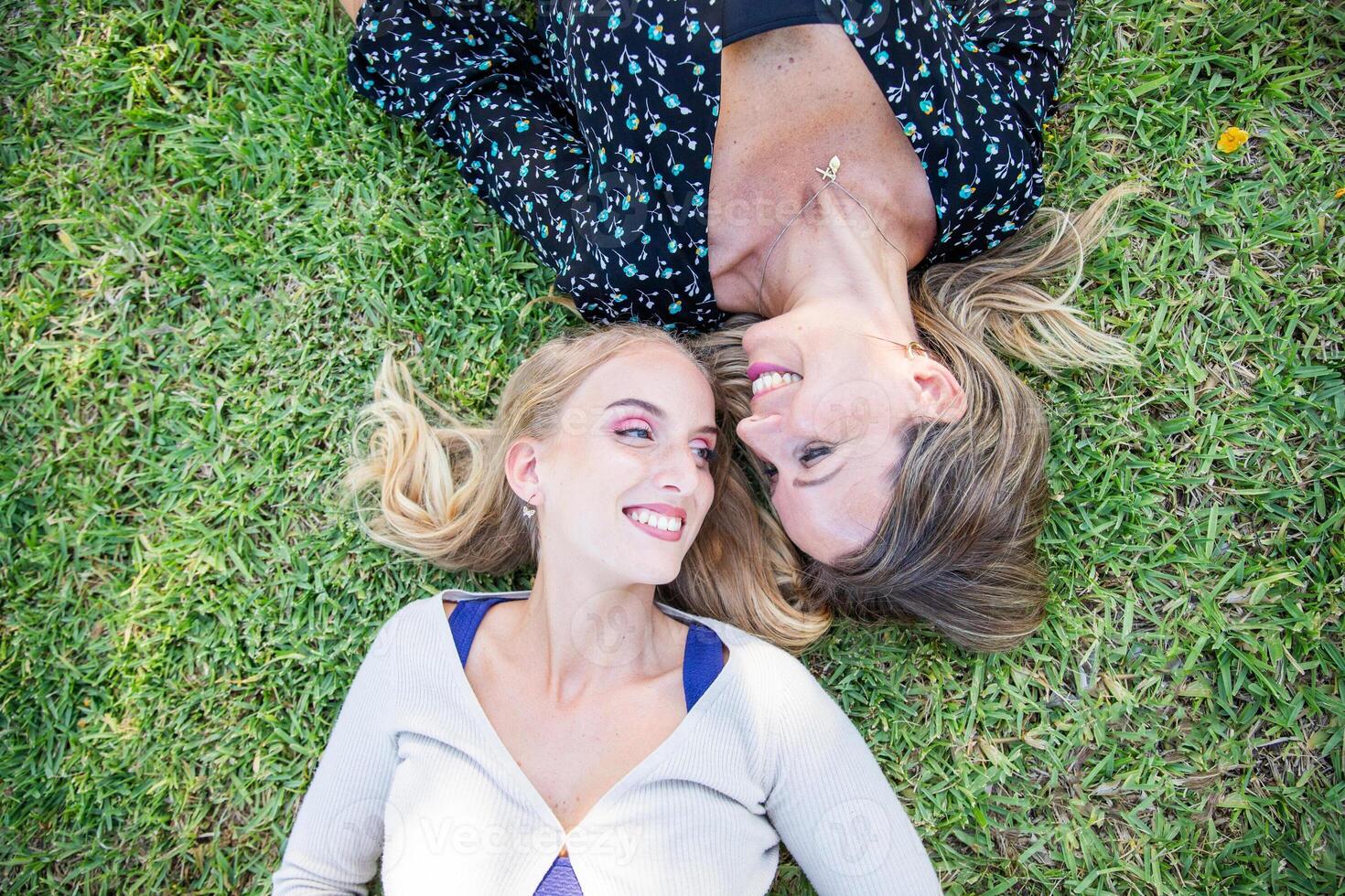 Mother and daughter laying on the grass smiling, photo from above with copy space